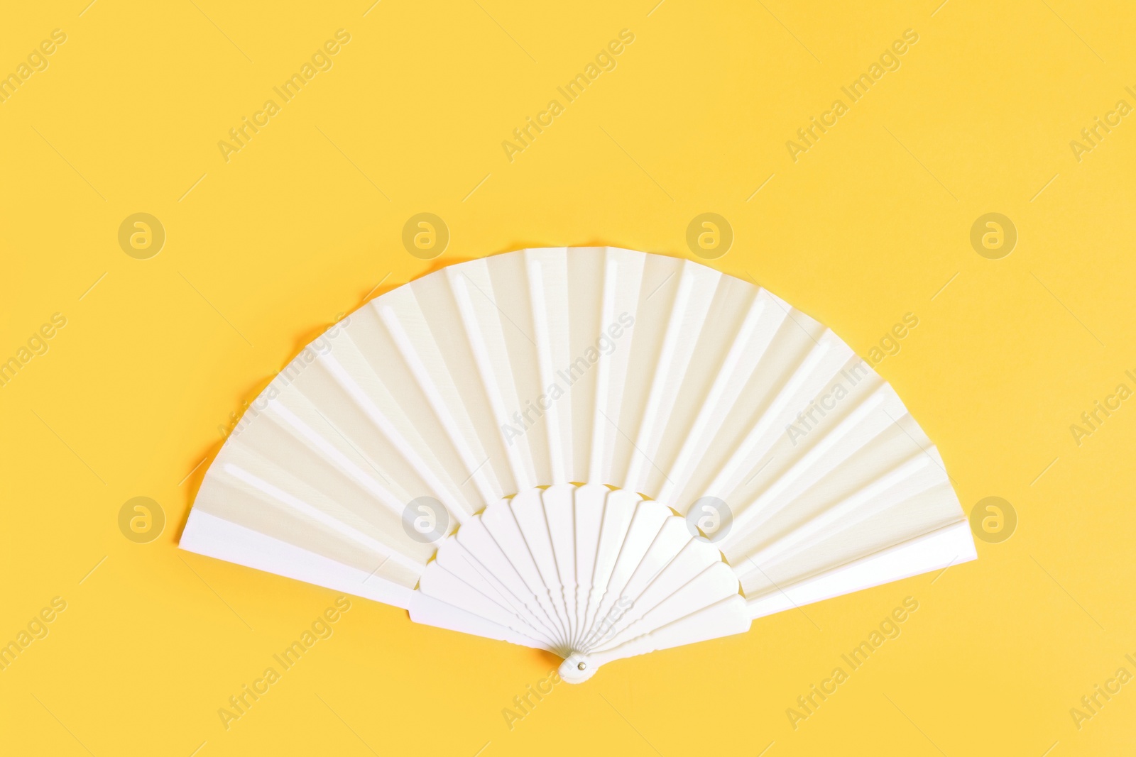 Photo of White hand fan on yellow background, top view