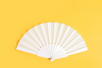 White hand fan on yellow background, top view