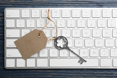 Key with blank tag and computer keyboard on blue wooden table, top view. Keyword concept