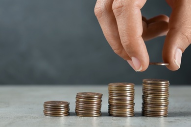 Young woman stacking coins on grey stone table, closeup view. Space for text