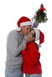 Photo of Happy man kissing his girlfriend under mistletoe bunch on white background