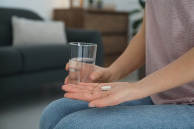 Photo of Young woman with abortion pill and glass of water indoors, closeup