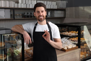 Photo of Happy seller showing OK gesture near showcase in bakery shop