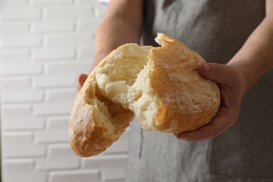 Photo of Man breaking loaf of fresh bread near white brick wall, closeup