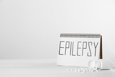Photo of Notebook with word Epilepsy and pills on white table, space for text