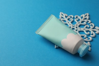 Photo of Tube of hand cream and snowflake on light blue background, space for text. Winter skin care