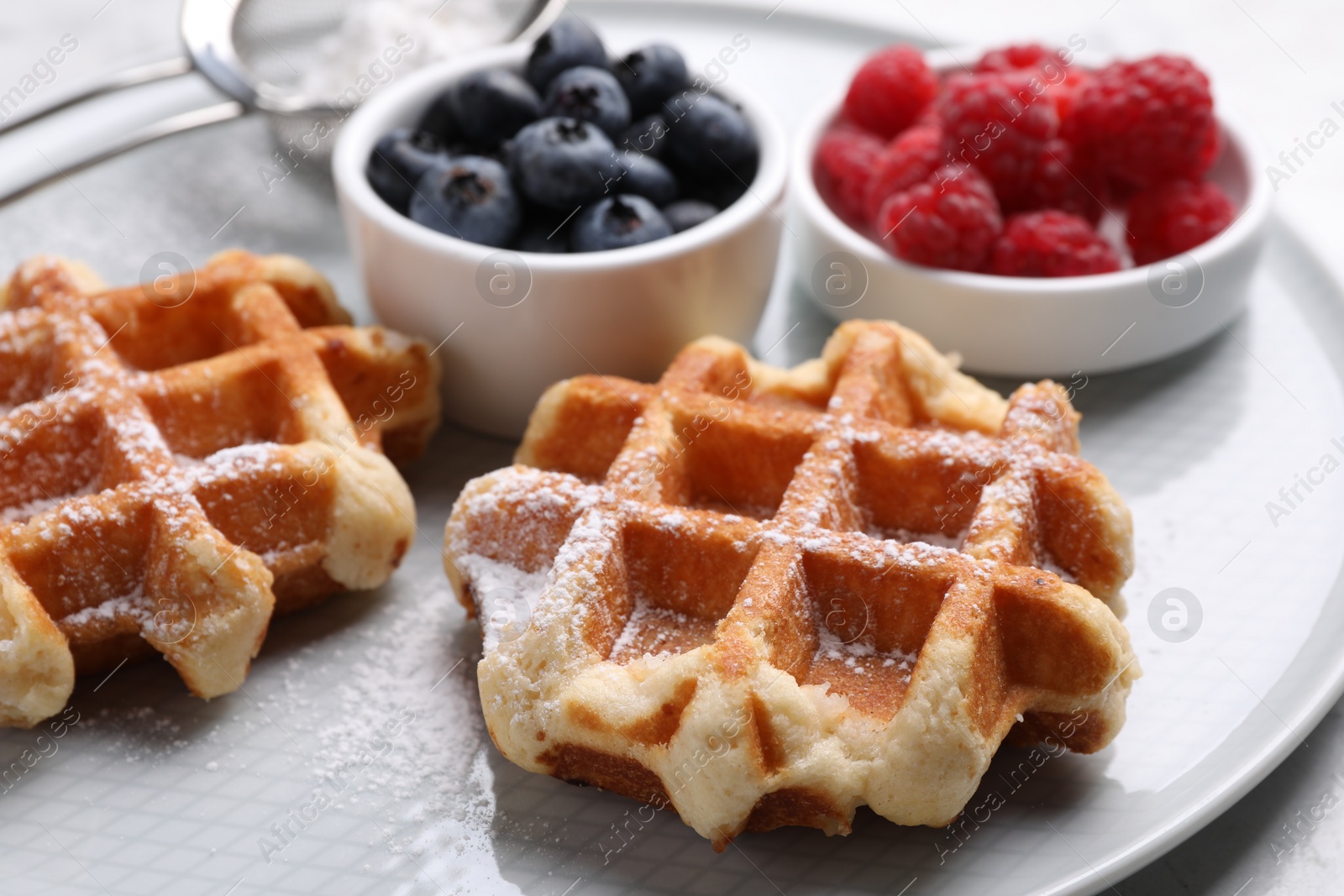 Photo of Delicious Belgian waffles with fresh berries and powdered sugar on plate, closeup