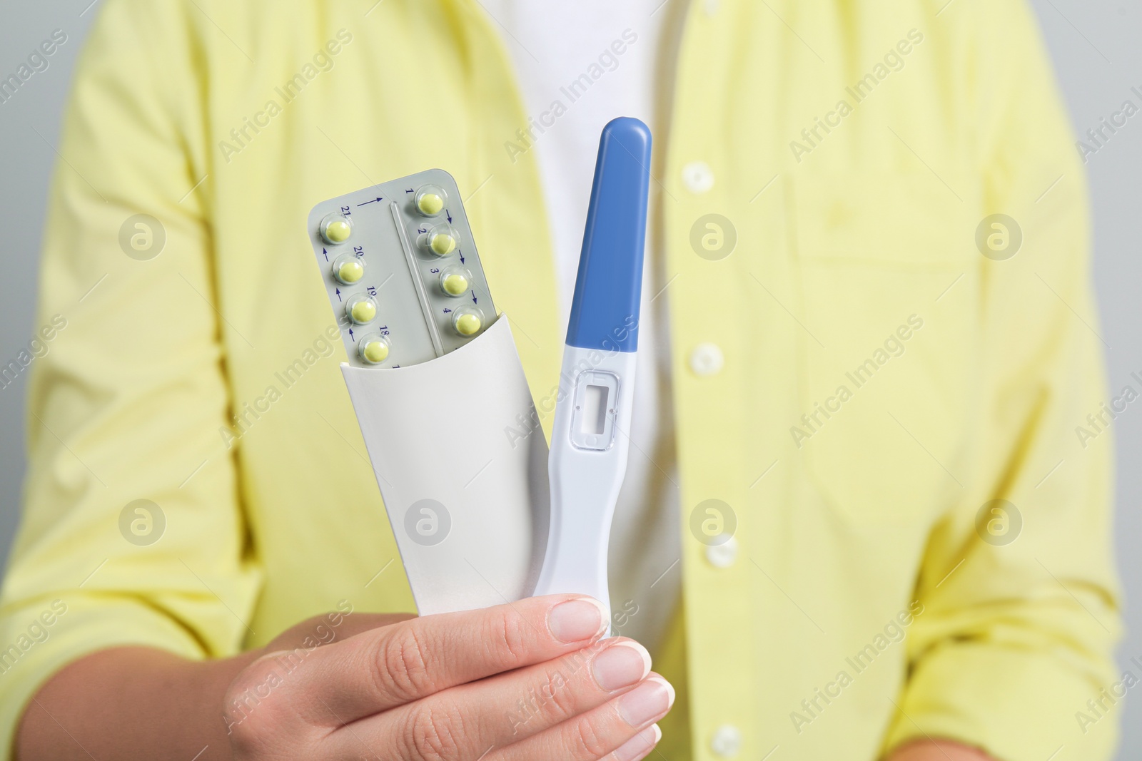 Photo of Woman holding birth control pills pregnancy test on grey background, closeup