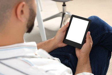 Man using e-book reader indoors, closeup view