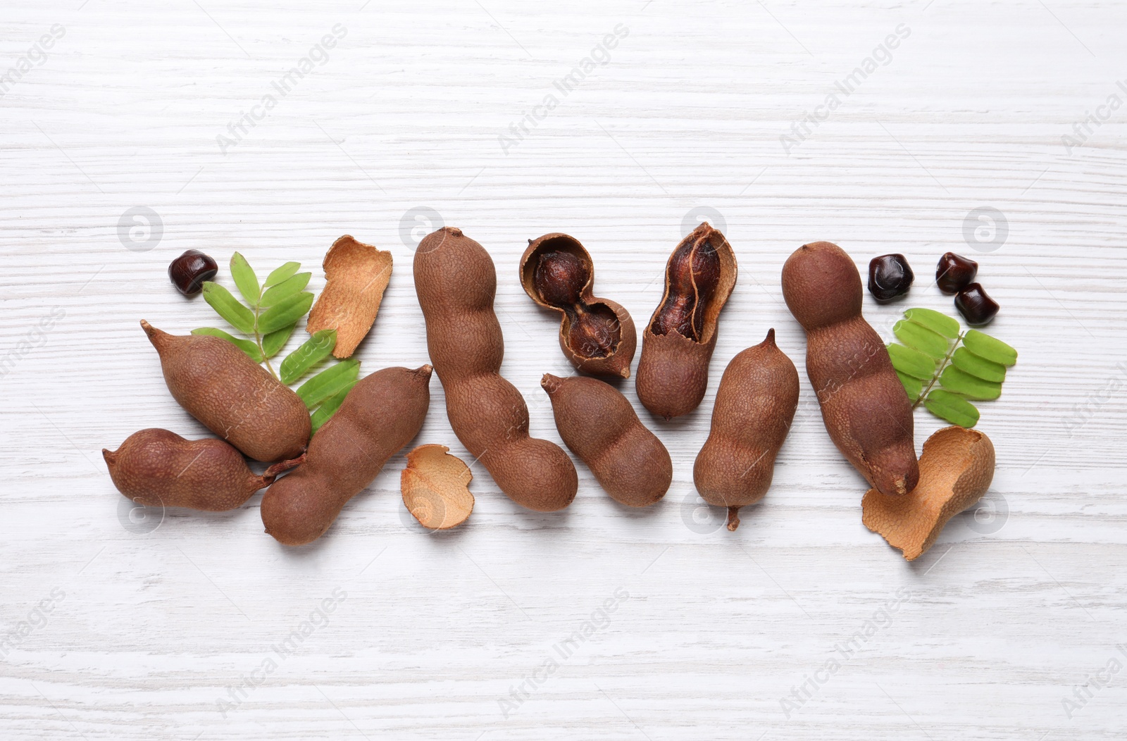 Photo of Delicious ripe tamarinds and leaves on white wooden table, flat lay