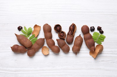 Delicious ripe tamarinds and leaves on white wooden table, flat lay