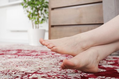 Woman sitting on carpet with pattern at home, closeup. Space for text