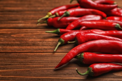 Photo of Fresh red chili peppers on wooden table with space for text