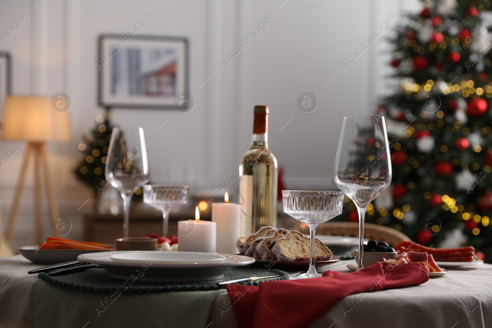 Photo of Christmas table setting with burning candles, appetizers and dishware in room