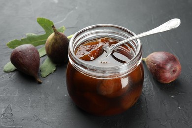 Photo of Jar of tasty sweet jam and fresh figs on black table