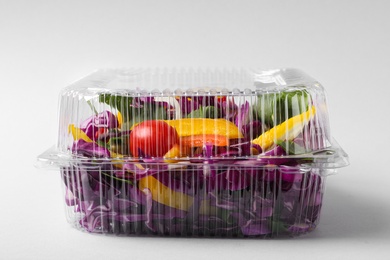 Plastic container with fresh salad on light grey background