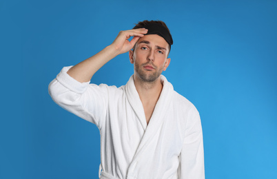 Photo of Sleepy young man in bathrobe on light blue background