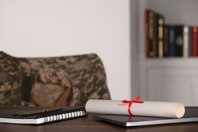 Photo of Notebook, laptop, pen, pencil and diploma on wooden table indoors. Military education