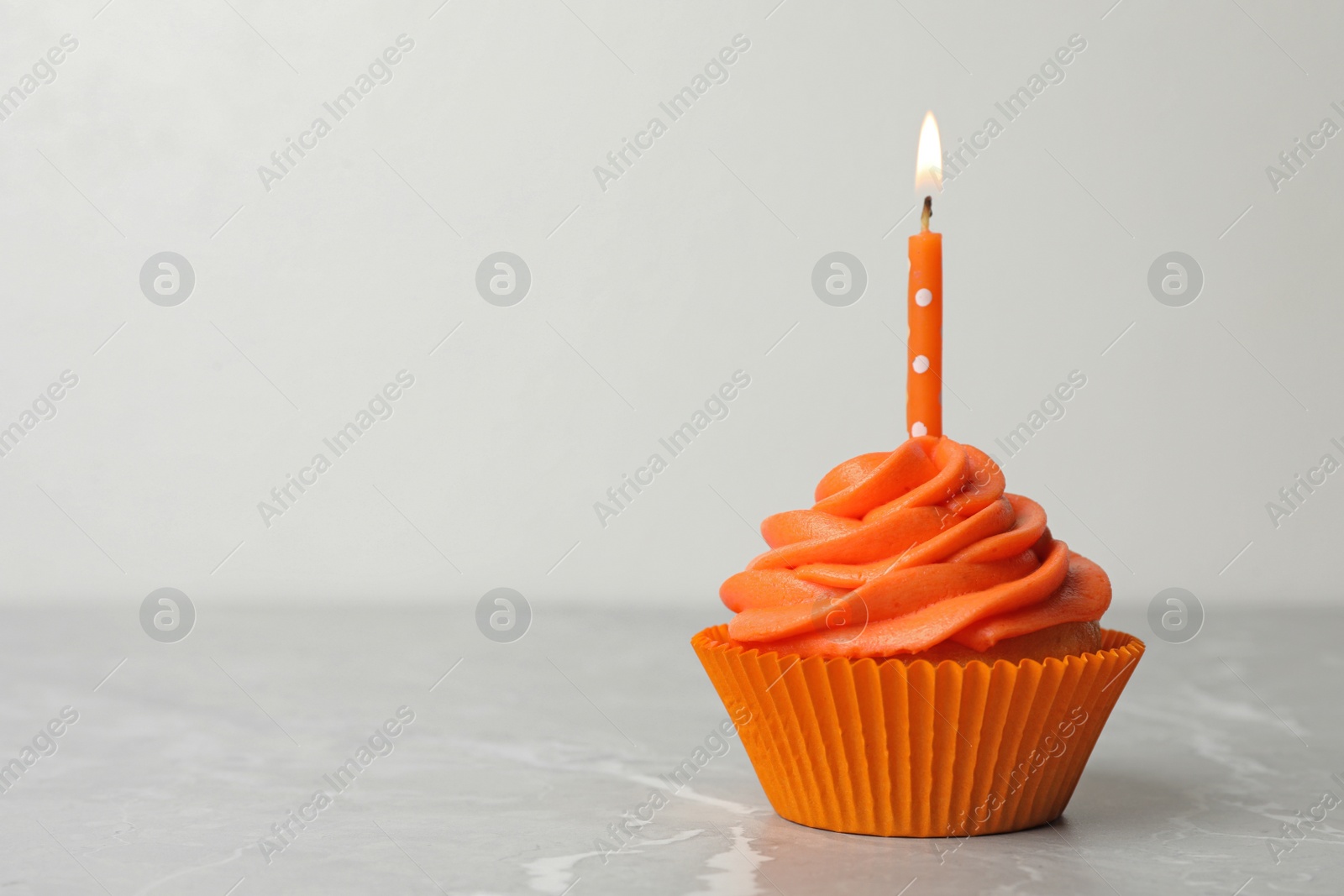 Photo of Delicious birthday cupcake with cream and burning candle on marble table. Space for text