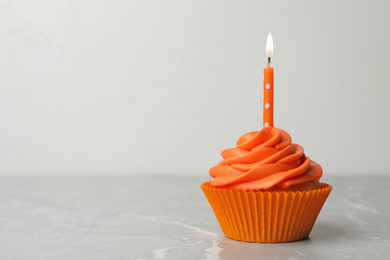 Delicious birthday cupcake with cream and burning candle on marble table. Space for text