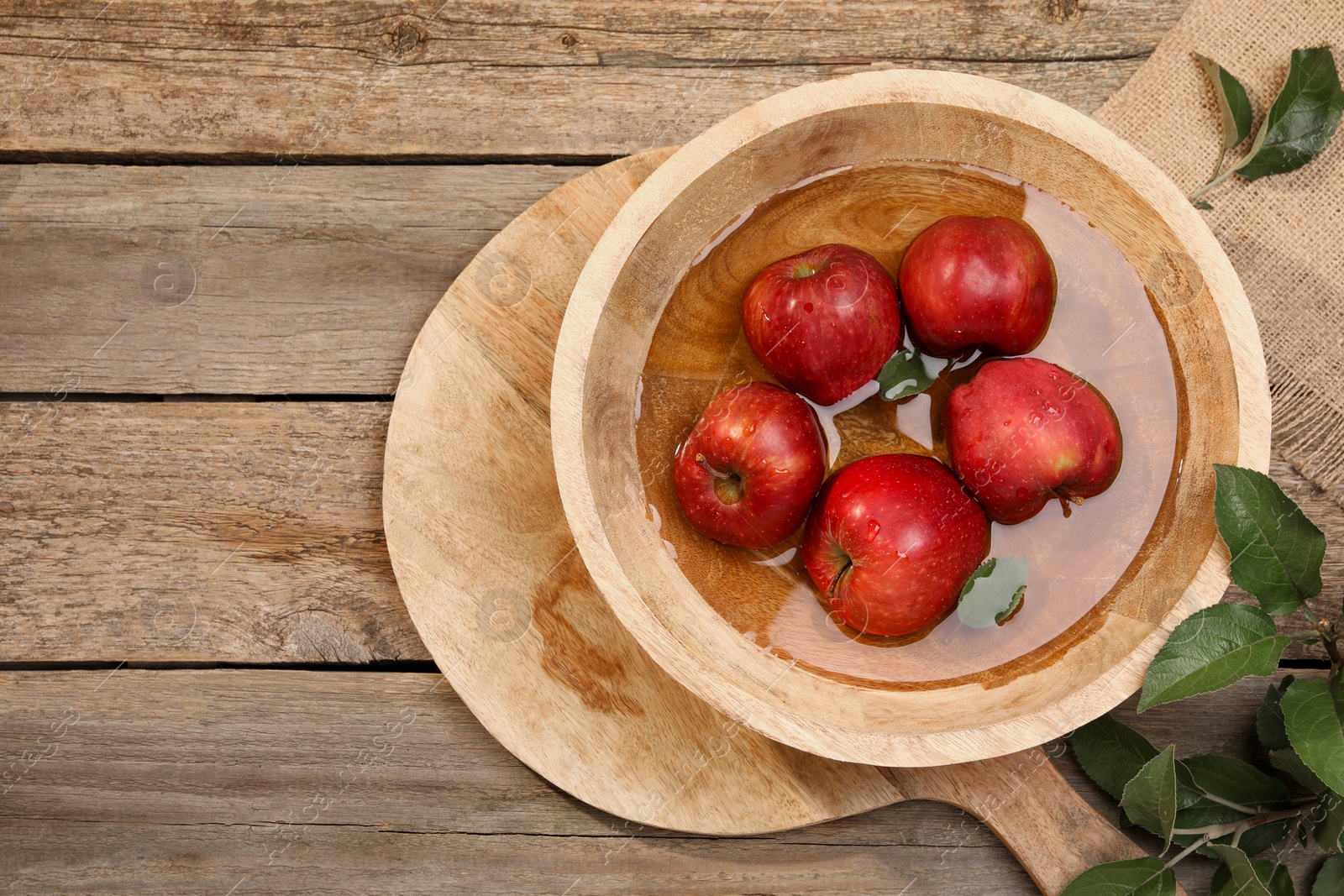 Photo of Fresh red apples in bowl with water and leaves on wooden table, flat lay. Space for text