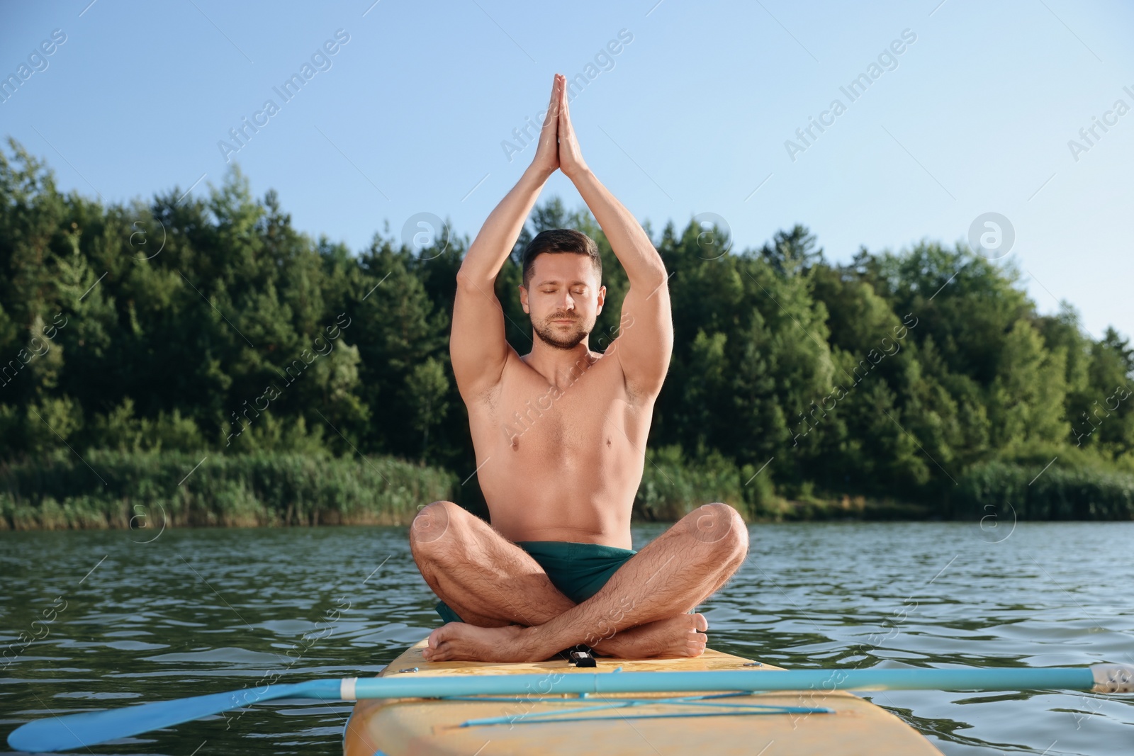 Photo of Man practicing yoga on color SUP board on river