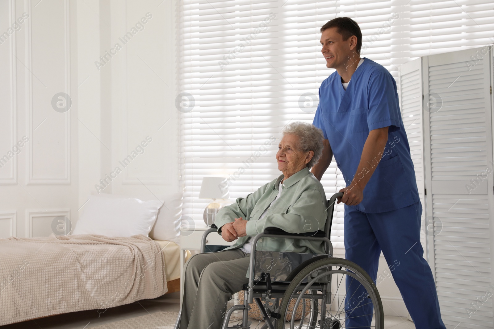 Photo of Caregiver assisting senior woman in wheelchair indoors. Home health care service