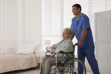 Photo of Caregiver assisting senior woman in wheelchair indoors. Home health care service