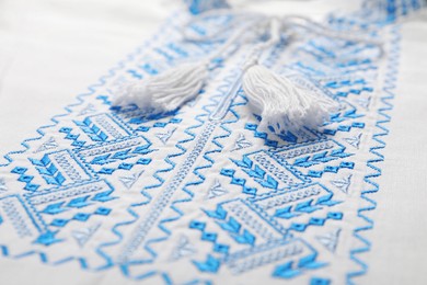 Photo of Beautiful light blue Ukrainian national embroidery on white fabric, closeup