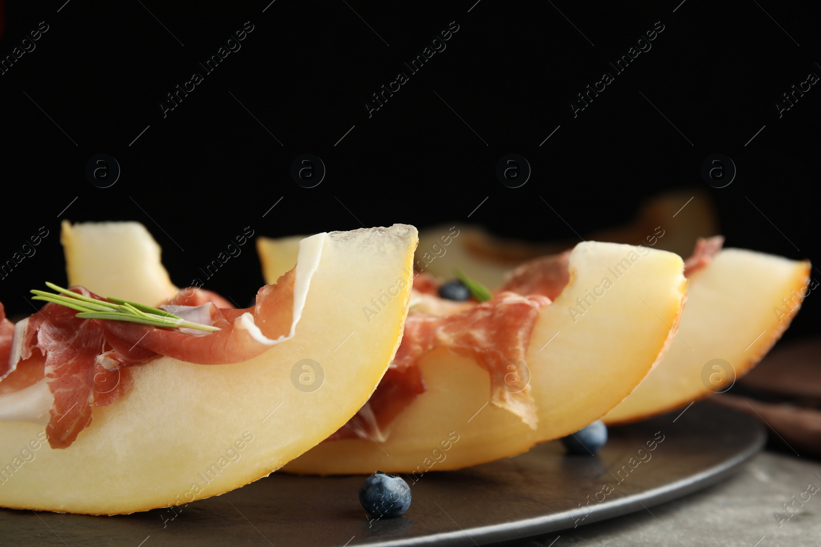 Photo of Melon with prosciutto, blueberries and rosemary on table