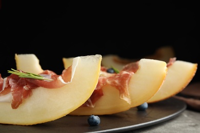 Photo of Melon with prosciutto, blueberries and rosemary on table