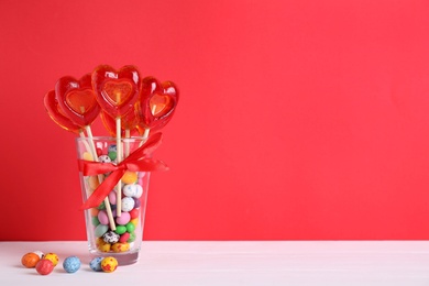 Photo of Delicious heart shaped lollipops and dragees on table. Space for text