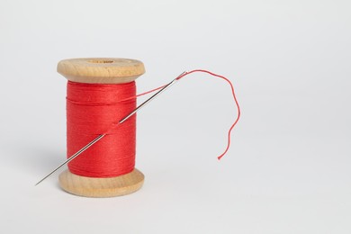 Red sewing thread with needle on white background