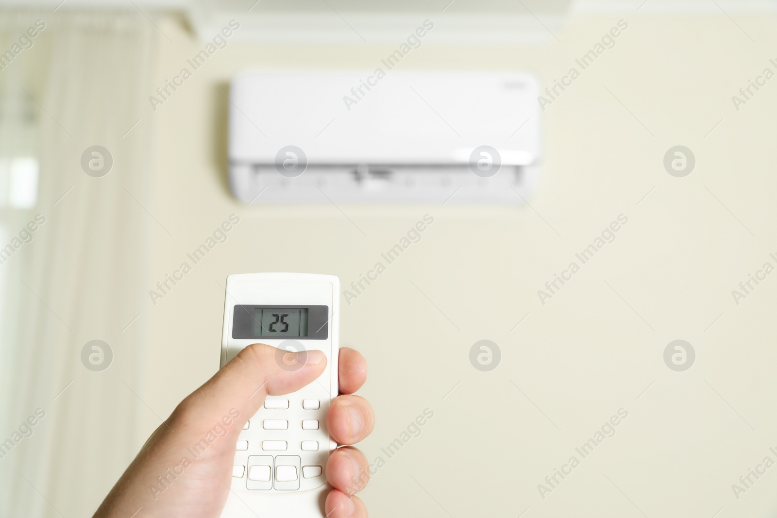 Photo of Man operating air conditioner with remote control indoors, closeup