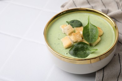 Delicious spinach cream soup with croutons in bowl on white tiled table. Space for text