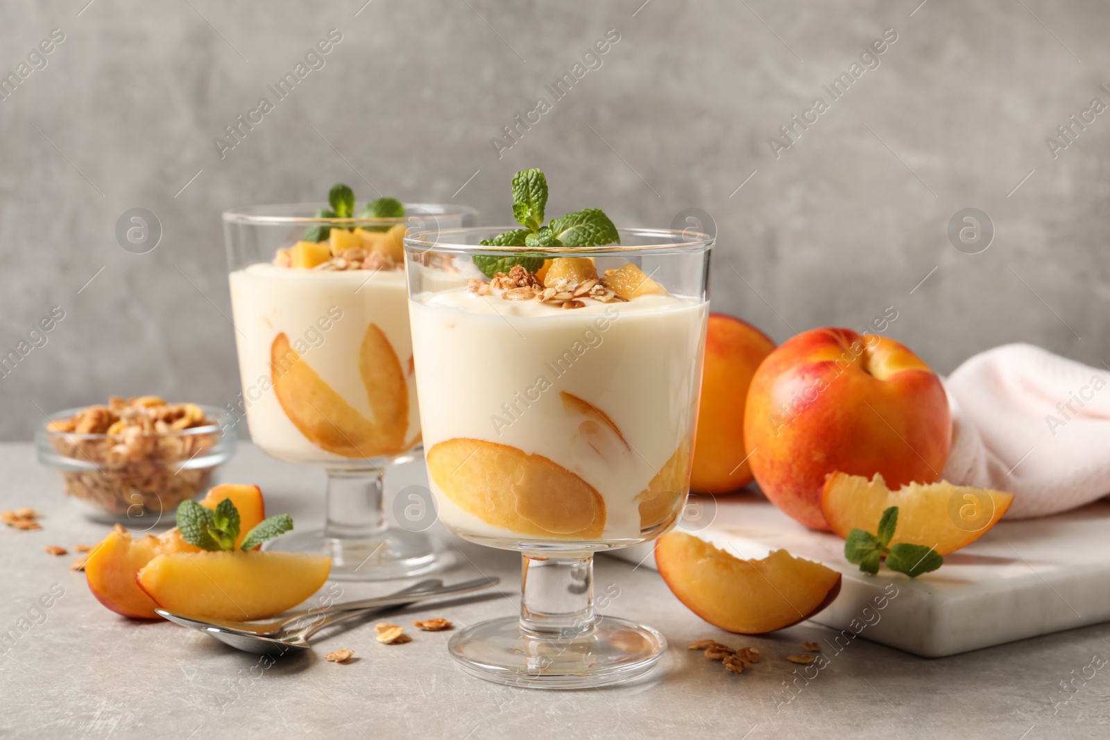 Photo of Tasty peach yogurt with granola, mint and pieces of fruits on light grey table