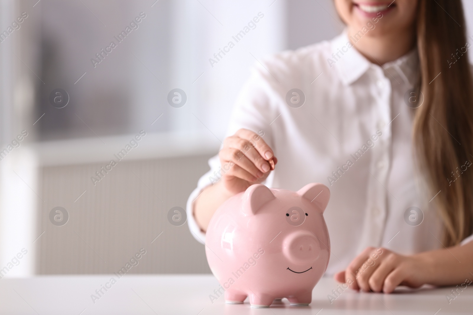 Photo of Woman putting coin into piggy bank at table indoors, closeup. Space for text