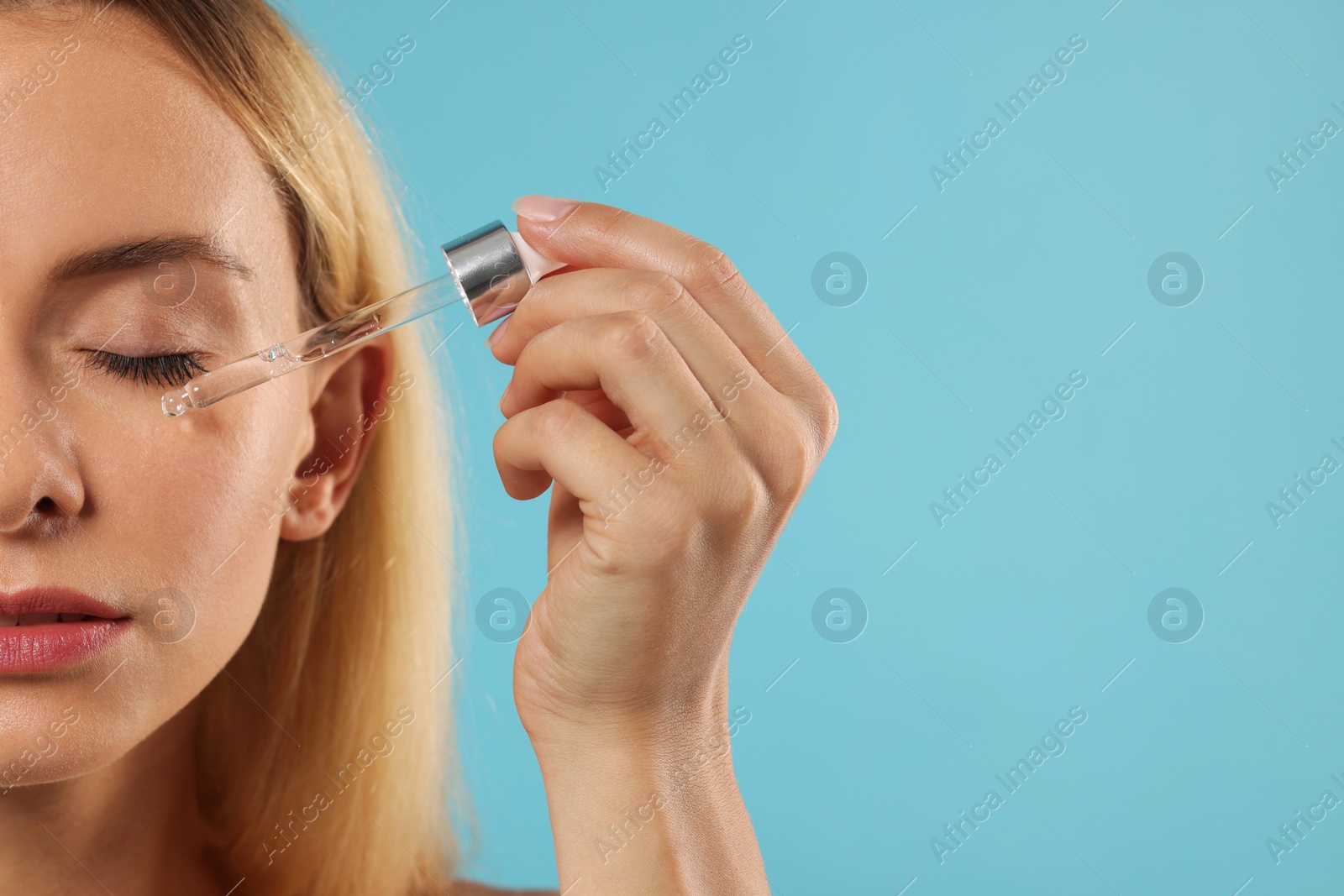 Photo of Beautiful woman applying cosmetic serum onto her face on light blue background, closeup. Space for text