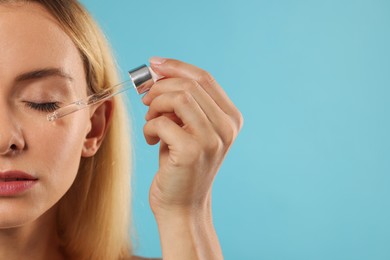 Beautiful woman applying cosmetic serum onto her face on light blue background, closeup. Space for text