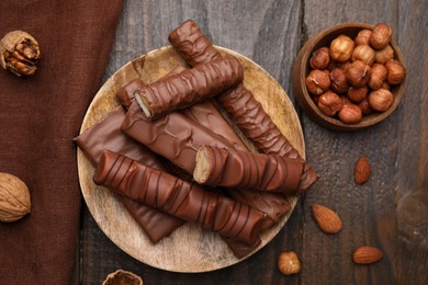 Photo of Different tasty chocolate bars and hazelnuts on wooden table, flat lay