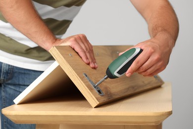 Photo of Man with electric screwdriver assembling furniture at table indoors, closeup