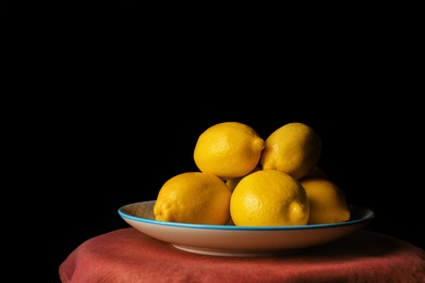 Photo of Plate with whole lemons on table against dark background