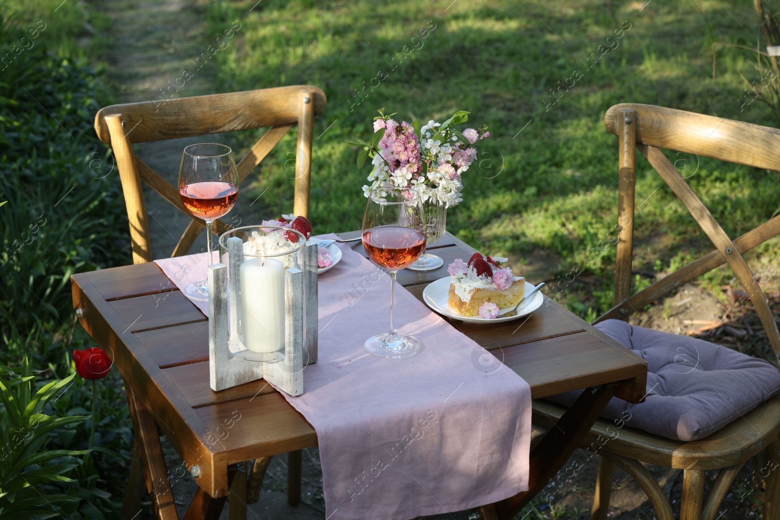 Photo of Vase with spring flowers, wine and cake on table served for romantic date in garden