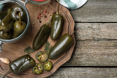 Pickled green jalapeno peppers and spices on wooden table, flat lay. Space for text