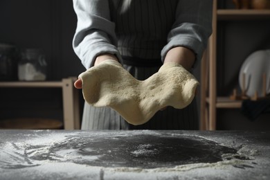 Woman tossing pizza dough at table in kitchen, closeup