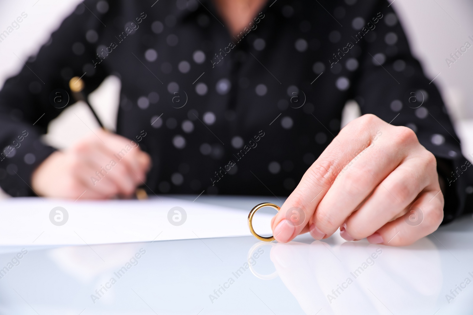 Photo of Woman with wedding ring signing divorce papers at table indoors, closeup. Space for text