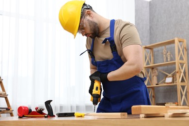 Young worker using electric drill at table in workshop