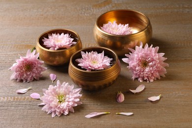 Photo of Tibetan singing bowls with water and beautiful flowers on wooden table
