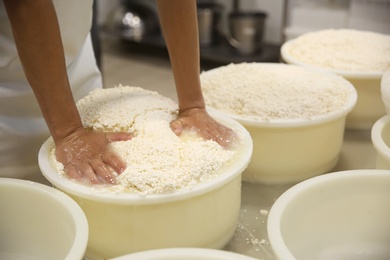 Photo of Worker pressing curd into mould at cheese factory, closeup