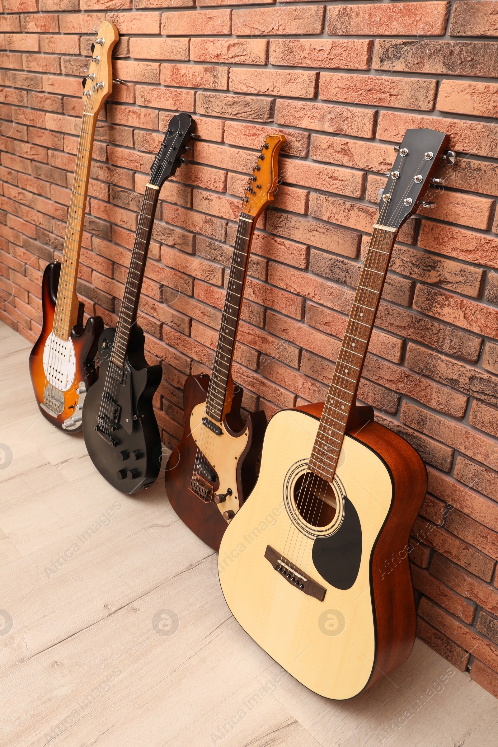 Photo of Modern electric and classical guitars near red brick wall indoors